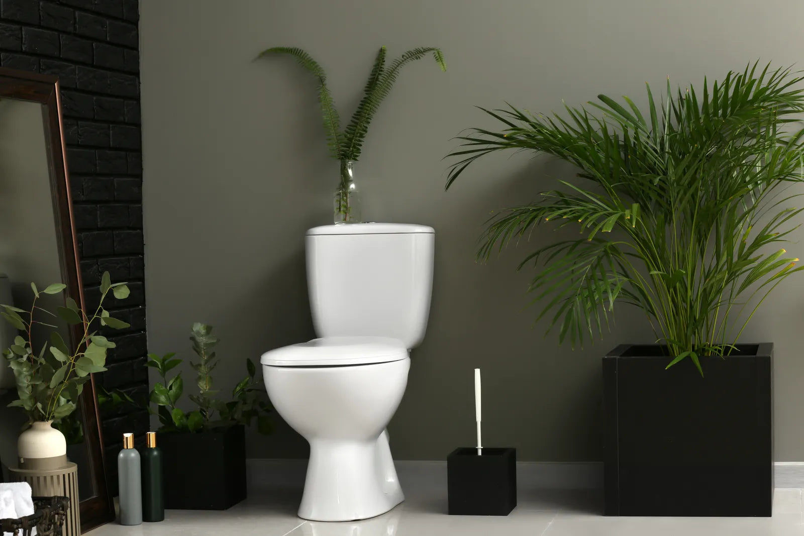 A clean, modern bathroom with a white toilet surrounded by lush green plants.
