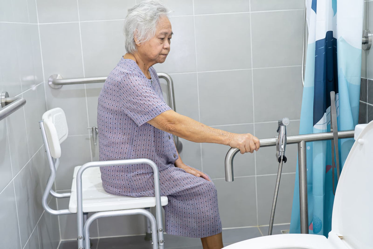 Older adult using an accessible toilet with grab bars in a home bathroom