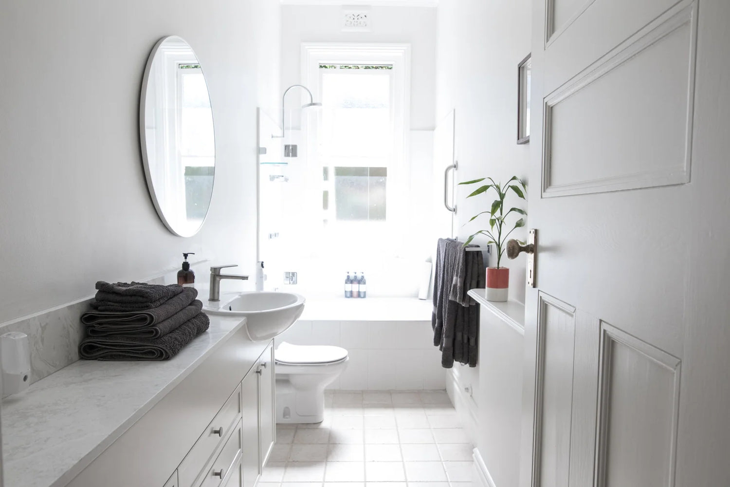 A bright, minimalist bathroom with white fixtures, a wall-mounted sink, and a toilet.