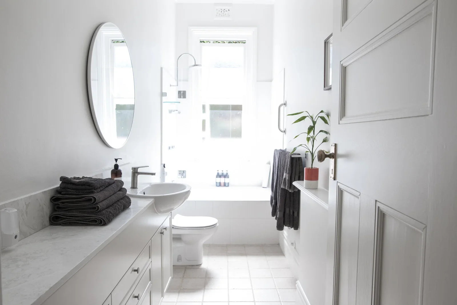 A bright, minimalist bathroom with white fixtures, a wall-mounted sink, and a toilet.