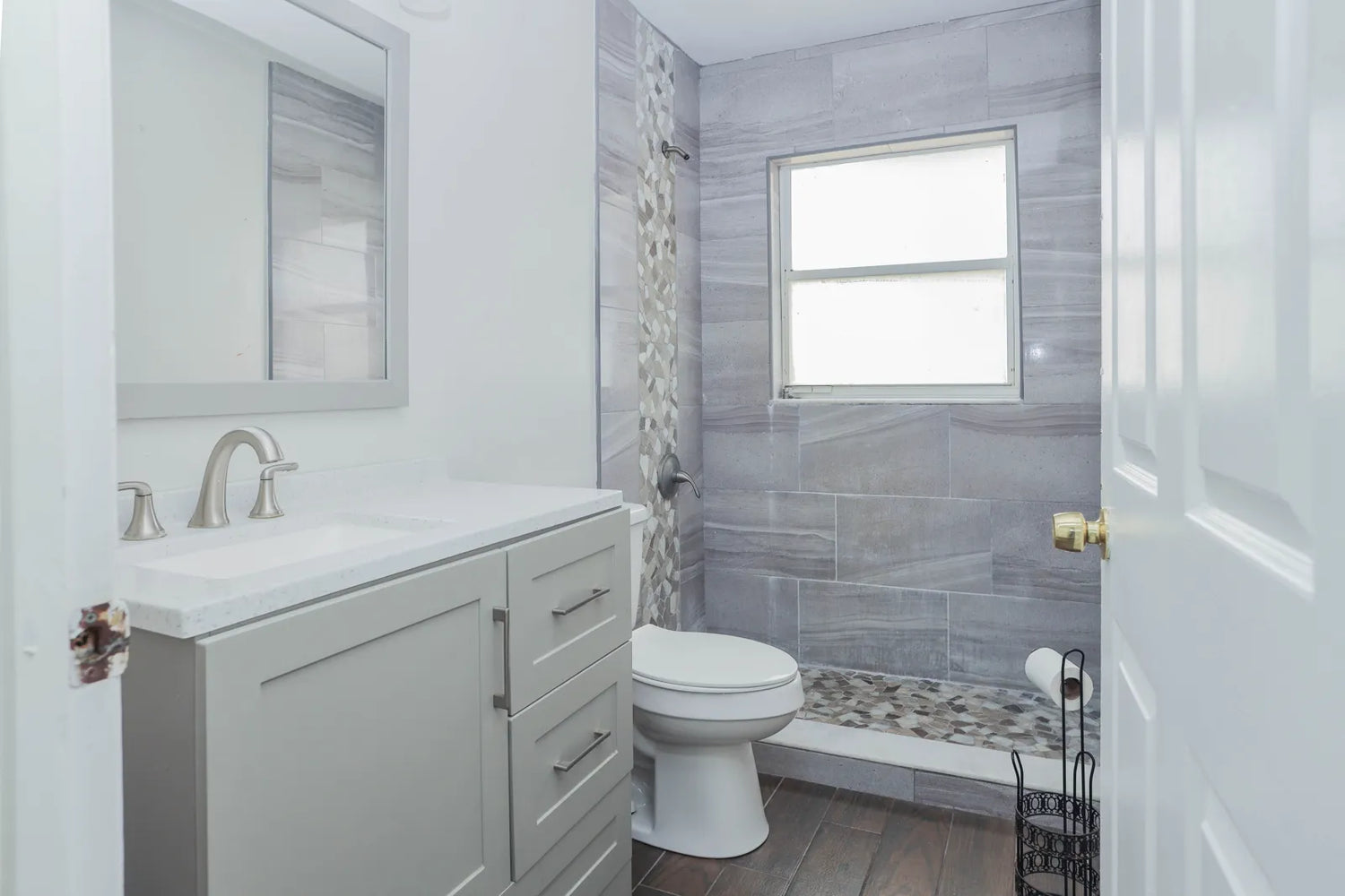 Modern gray-and-white bathroom with toilet, vanity, and tiled shower area.