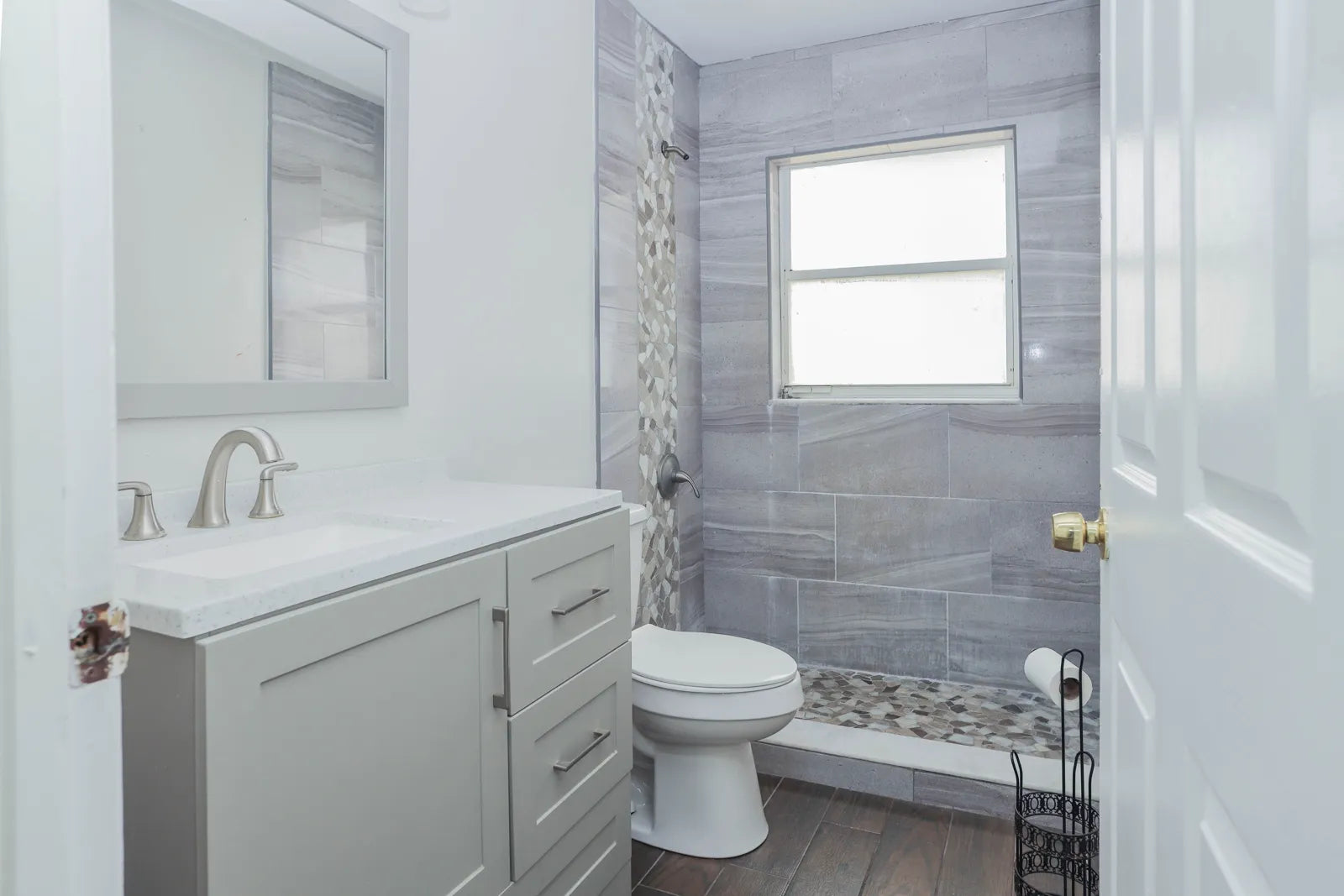 Modern gray-and-white bathroom with toilet, vanity, and tiled shower area.