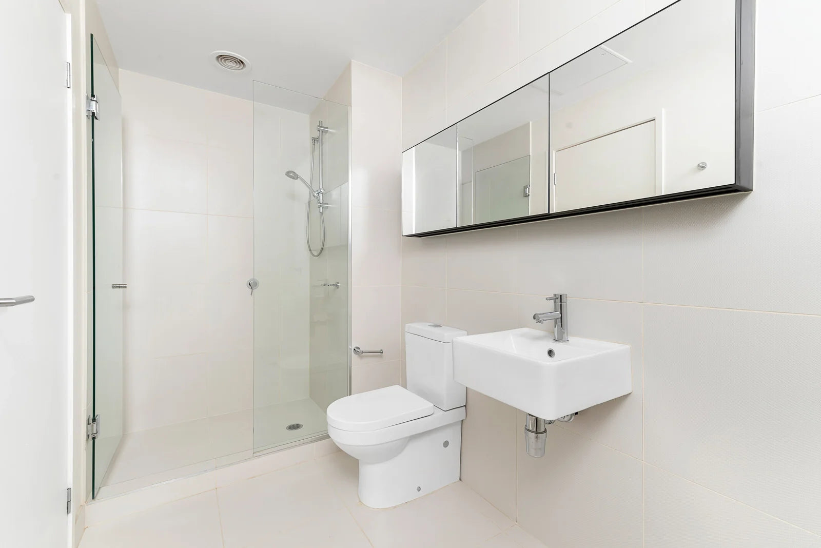 A modern bathroom featuring a standard toilet alongside a wall-mounted sink and glass shower.