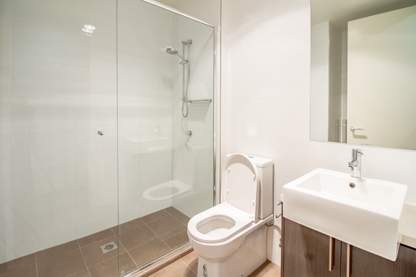 This bright contemporary bathroom features a full clear glass shower partition, white toilet and compact wall-mounted sink.