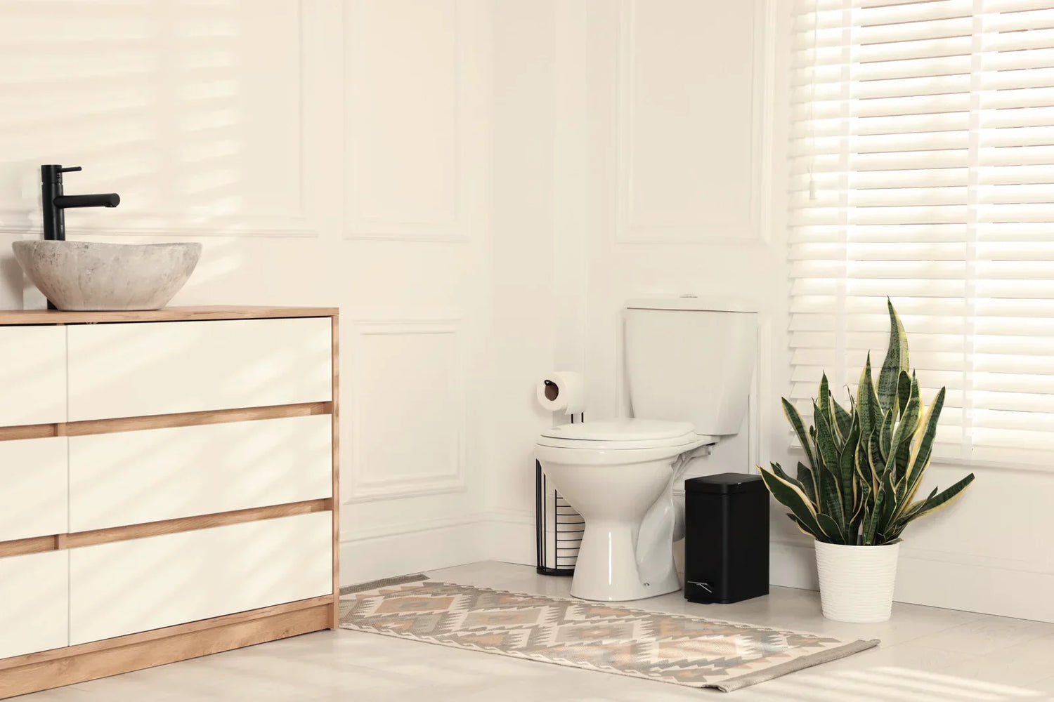 A bright modern bathroom with a white high-efficiency toilet, vanity, and plant, showcasing a clean home setting.