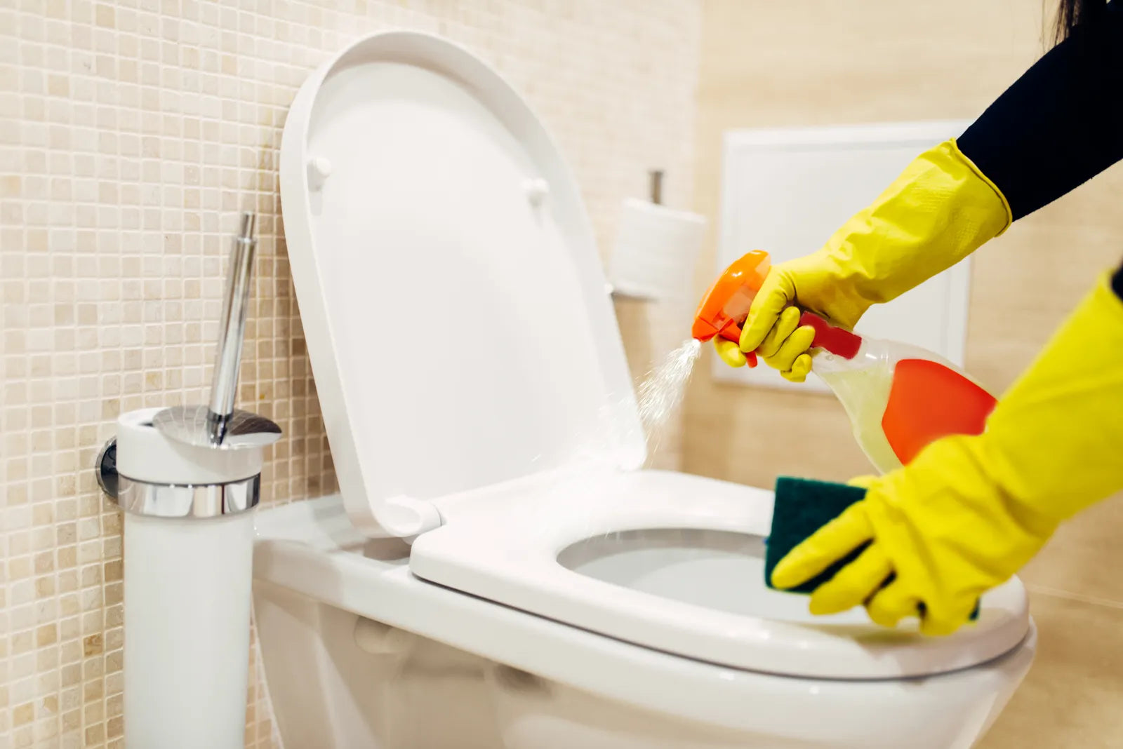 Person cleaning a toilet with spray and sponge, demonstrating manual cleaning steps that apply to bidet nozzle descaling.