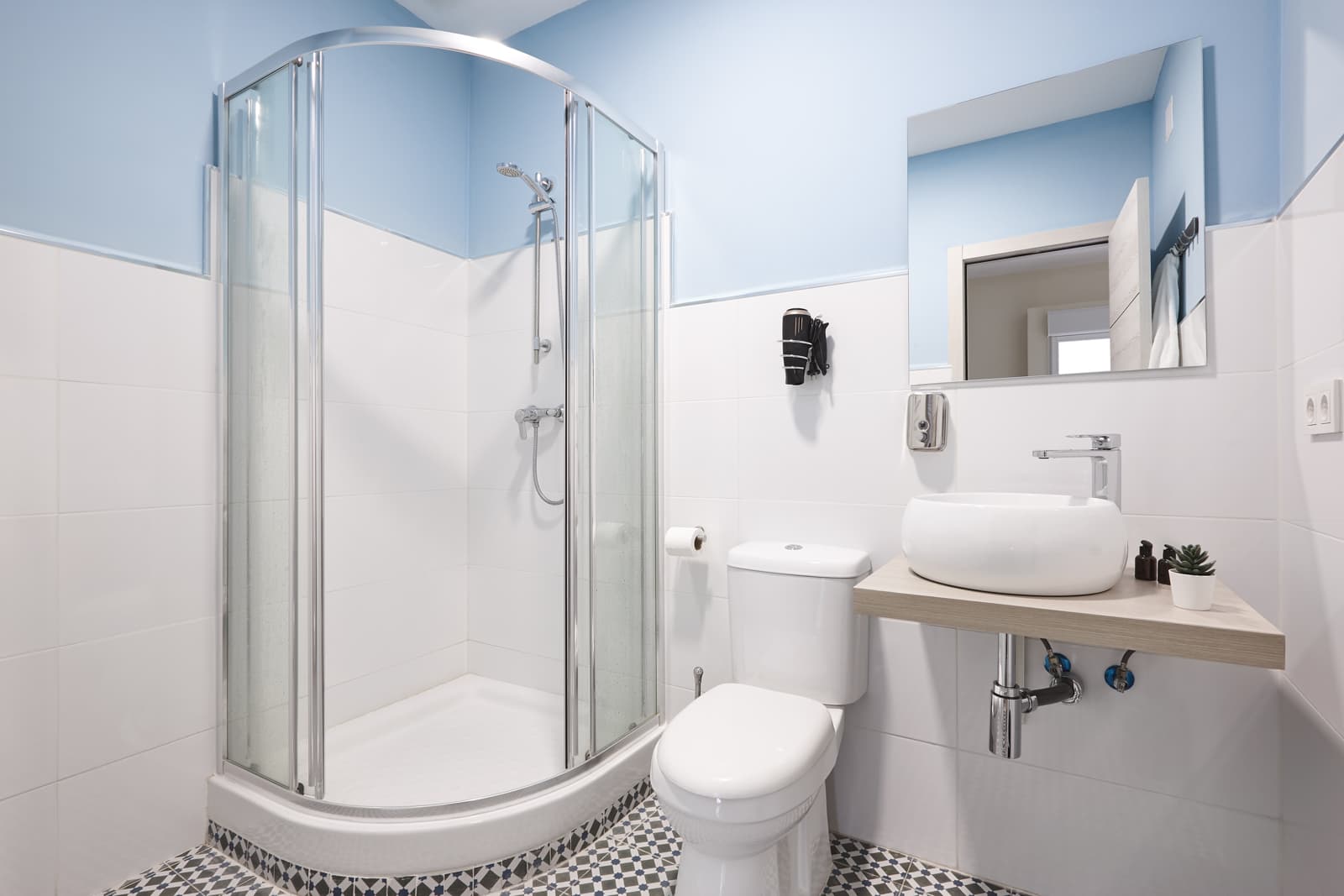Bright contemporary bathroom featuring a neo angle curved glass corner shower, white toilet, vessel sink and patterned floor tiles.