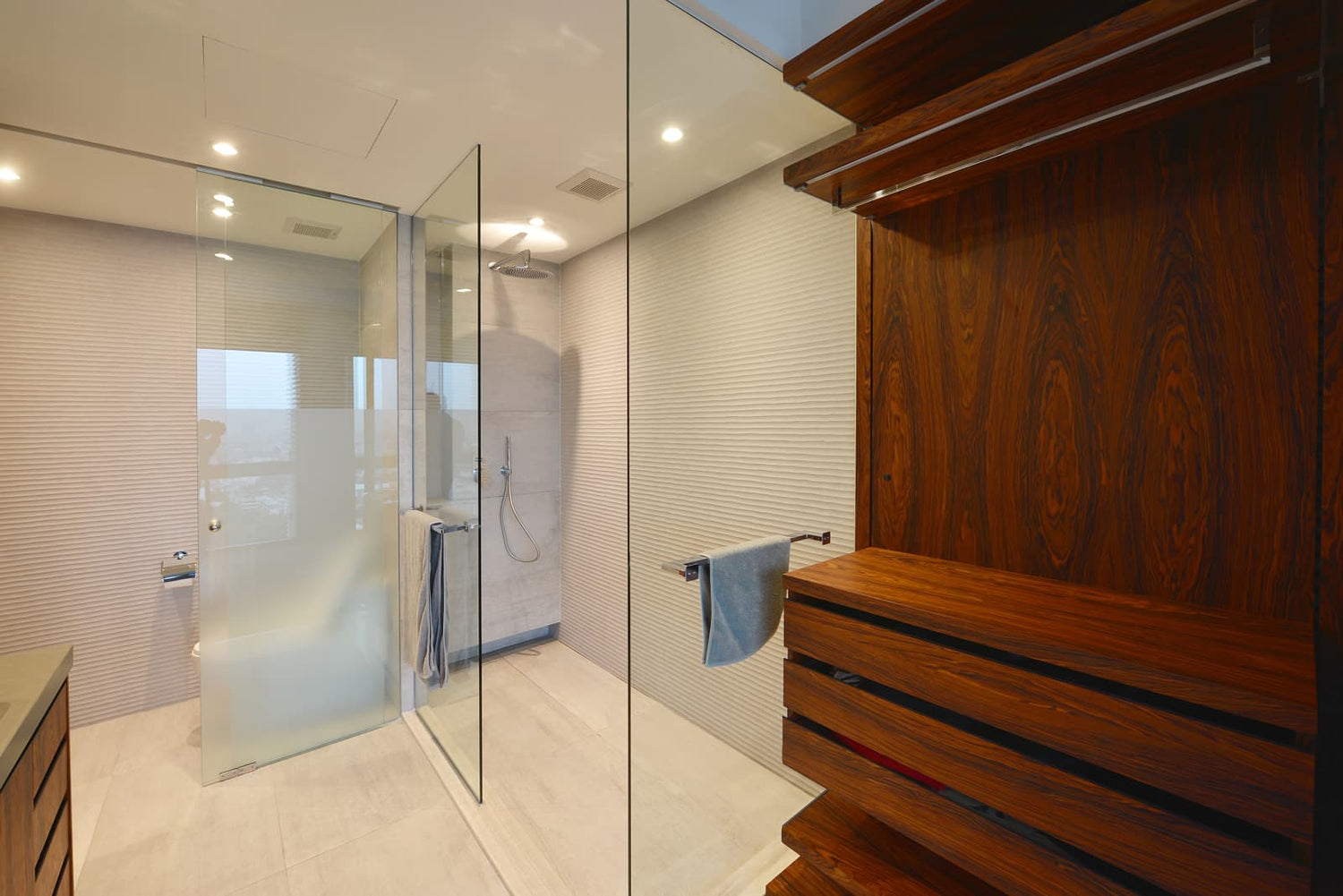 Luxury contemporary bathroom featuring frameless shower enclosure with partial frosted privacy glass panels for visual screening.