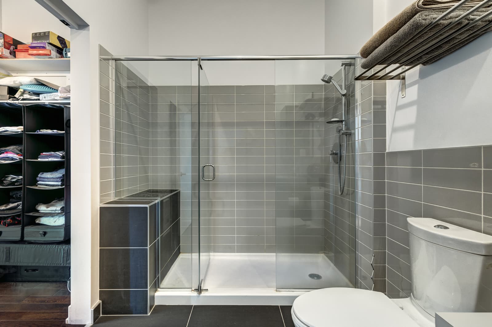 Spacious curbless shower space with frameless sliding clear glass door, demonstrating level entry design in a contemporary tiled bathroom.