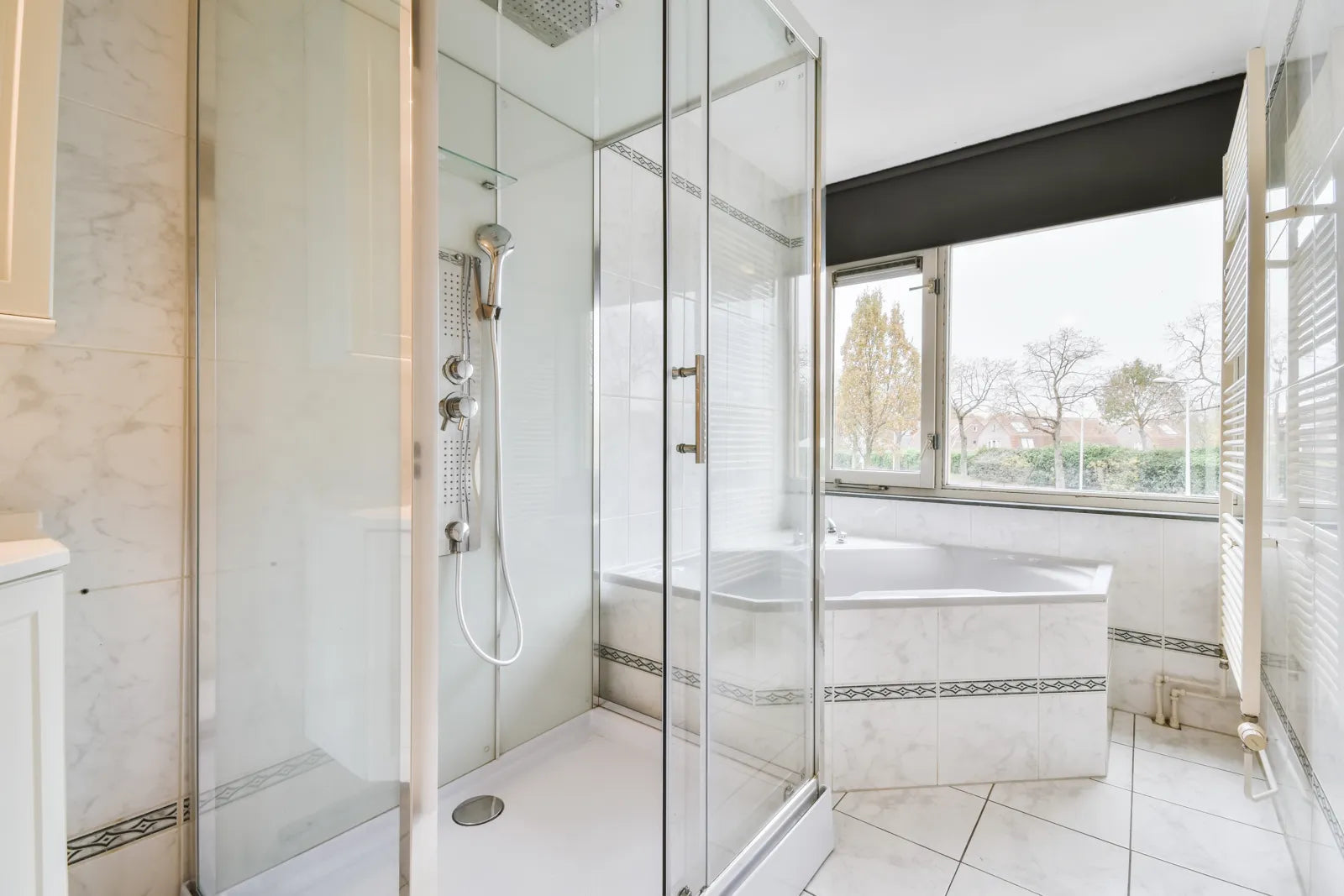 Bright, neutral-toned modern bathroom with a glass-enclosed shower and bathtub, natural light filtering through the window.