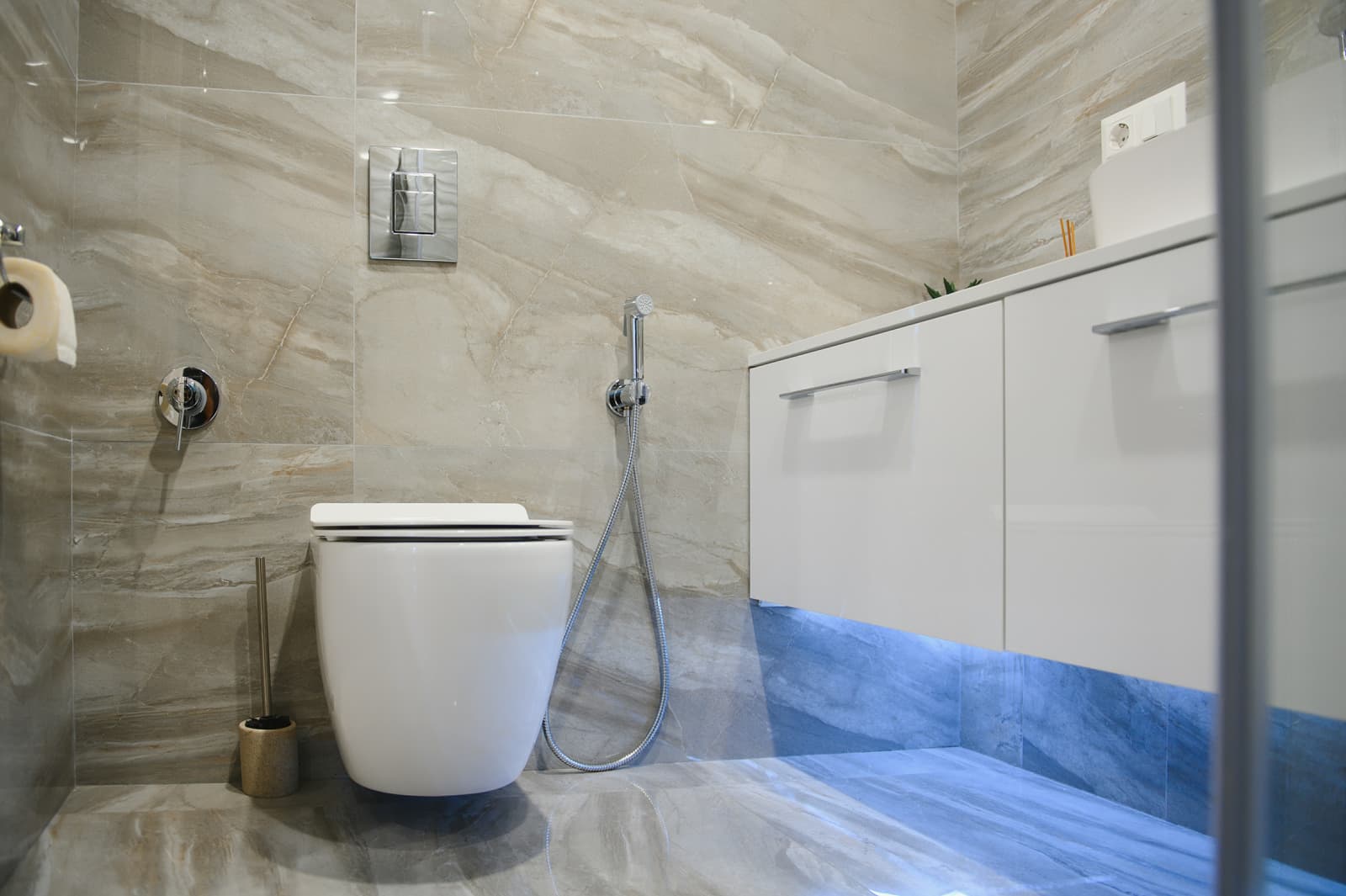 Sleek wall-hung smart toilet inside a modern tiled guest bathroom, paired with floating vanity and built-in bidet sprayer for visitor hygiene.