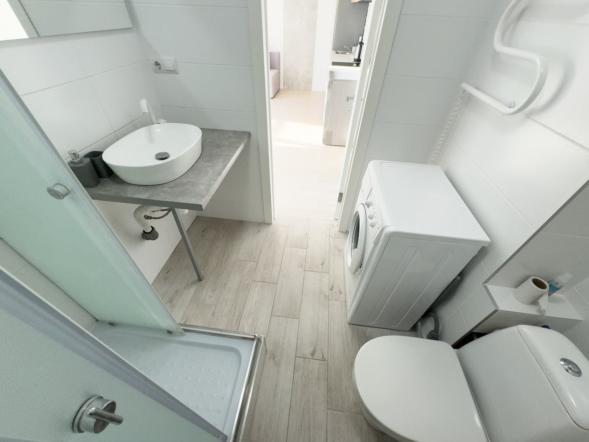 Compact bathroom with a toilet, shower, sink, and washing machine arranged in a narrow space