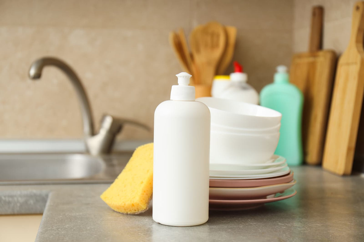 White pump soap dispenser beside stacked dishes and a sponge near the kitchen sink.