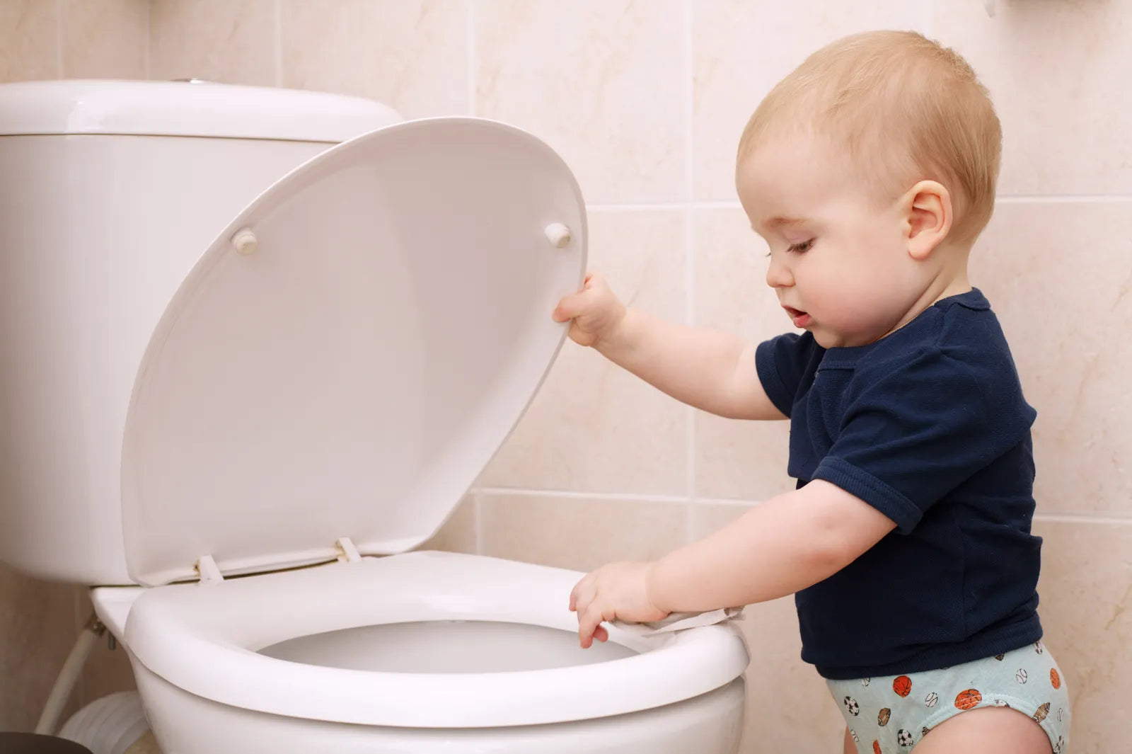 A toddler interacting with a standard height toilet in a bathroom, demonstrating the usability of lower toilets for young children.