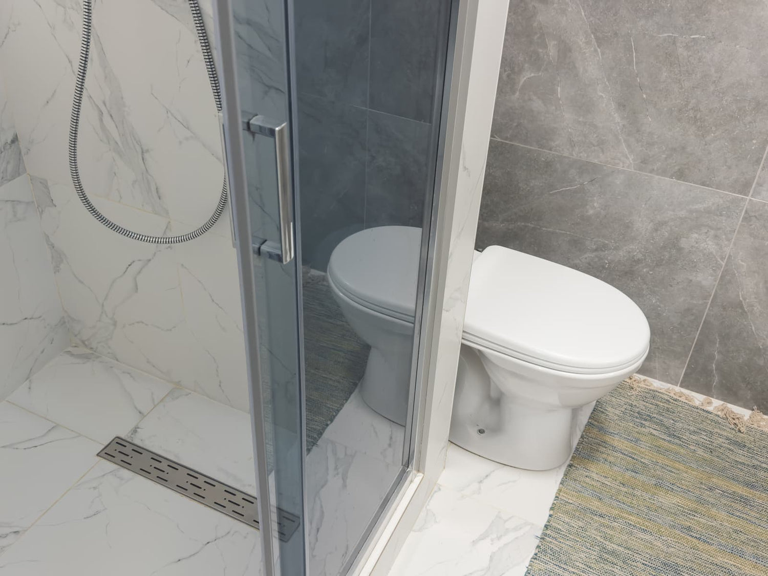 Modern bathroom with sliding tinted glass shower enclosure positioned beside the toilet, showing space planning for compact layouts.