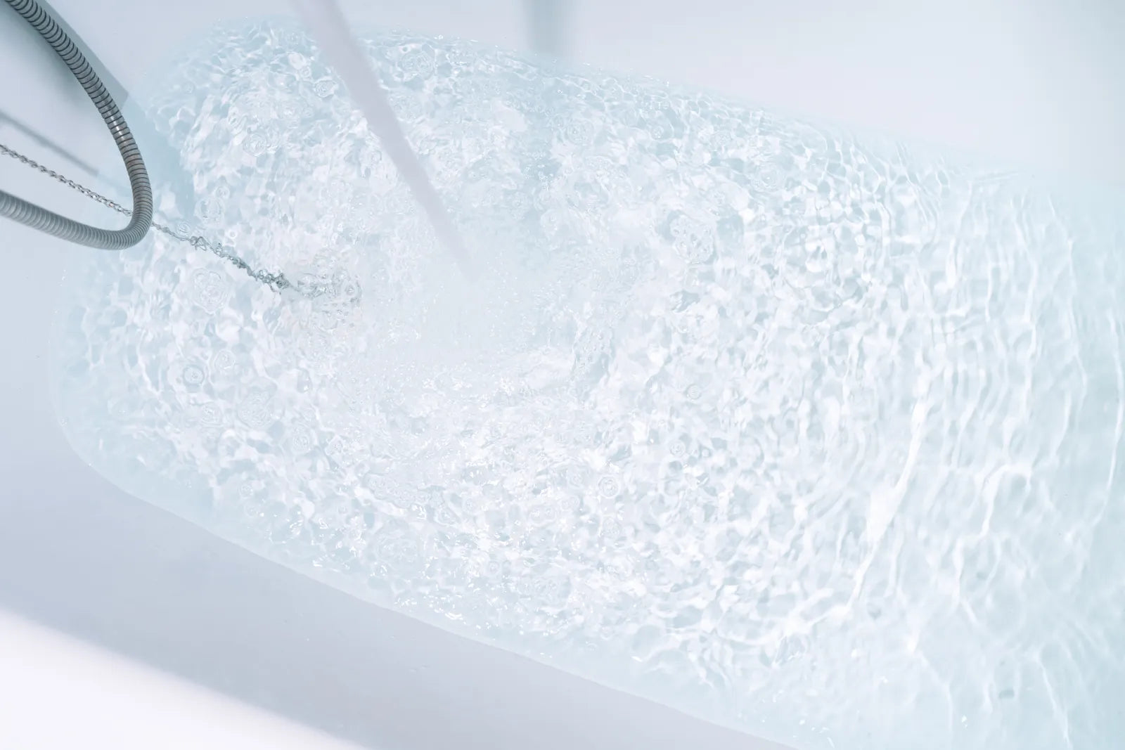 Close-up of clear water filling a white bathtub, showing bubbly surface and metal hose, illustrating initial water flow before slow drainage issues.