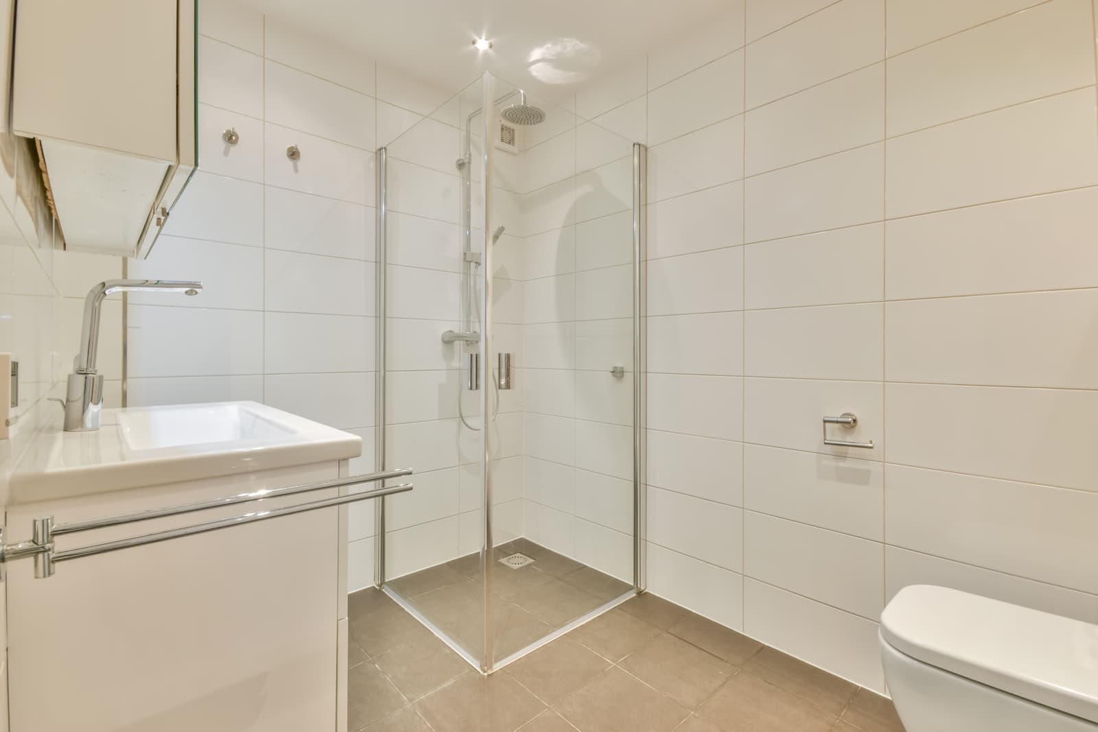 Bright minimalist bathroom featuring a frameless glass corner shower door, showcasing a clean accessible shower layout for home accessibility renovations.