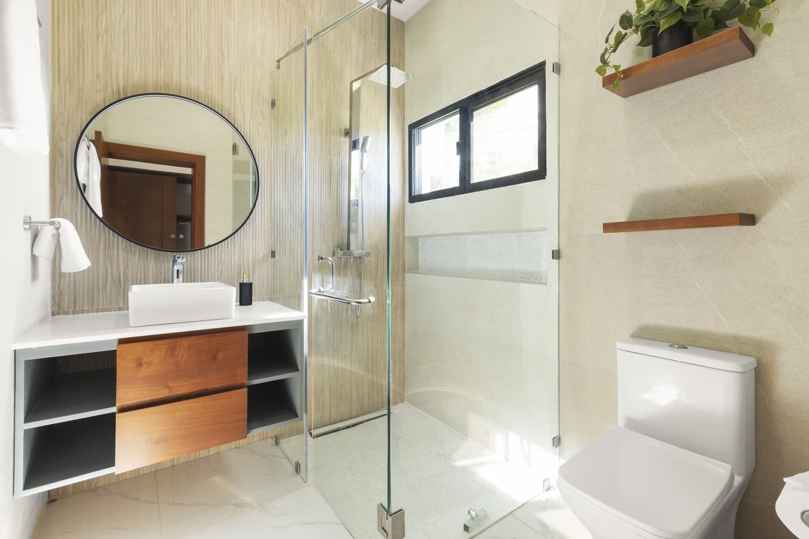 Bright contemporary bathroom featuring a frameless clear glass shower door paired with light textured wall tiles and wooden vanity.