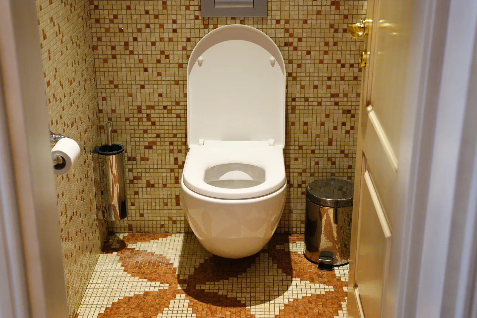 Wall-mounted compact toilet in a tiny mosaic-tiled bathroom