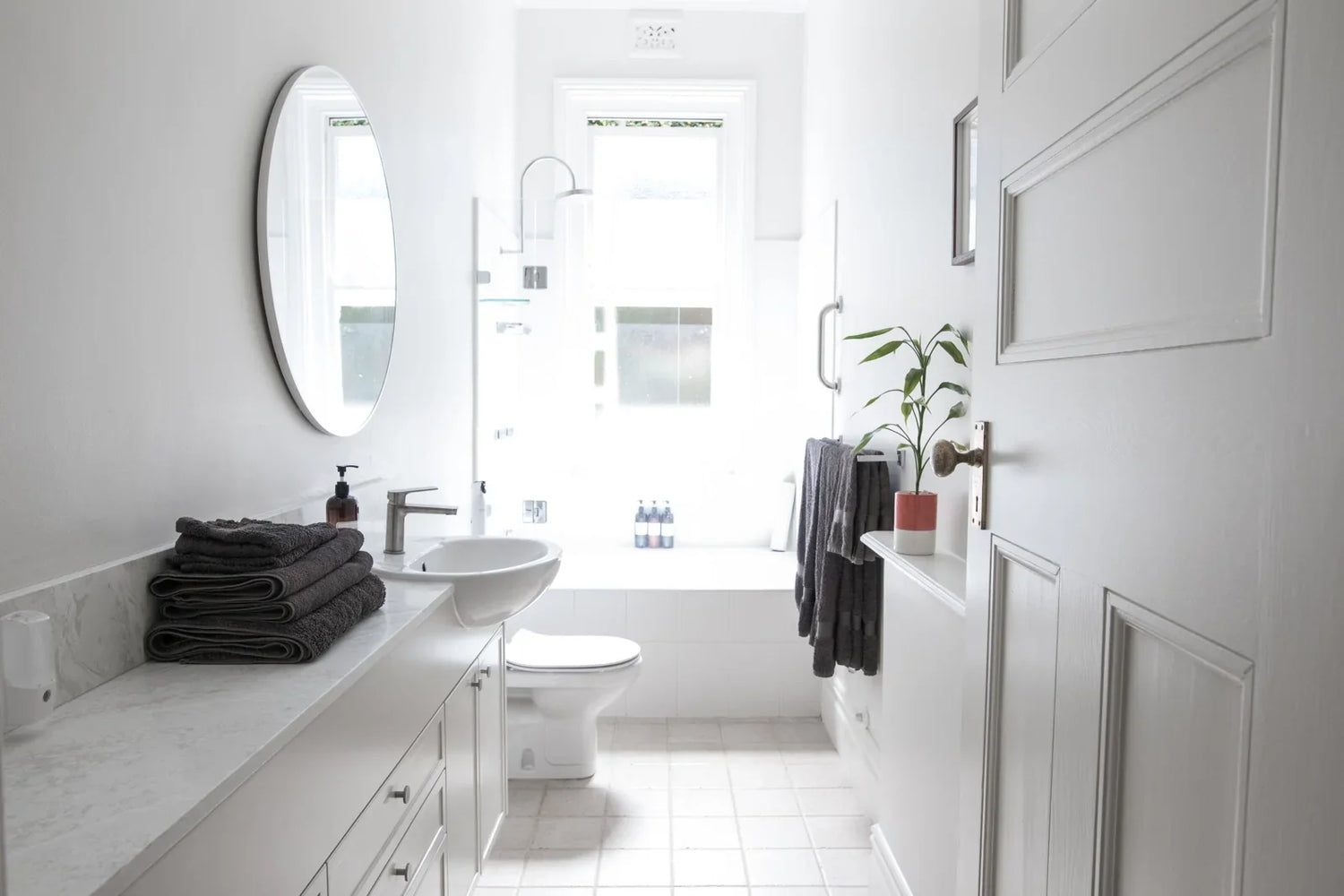 A bright, minimalist bathroom with white fixtures, a wall-mounted sink, and a toilet.