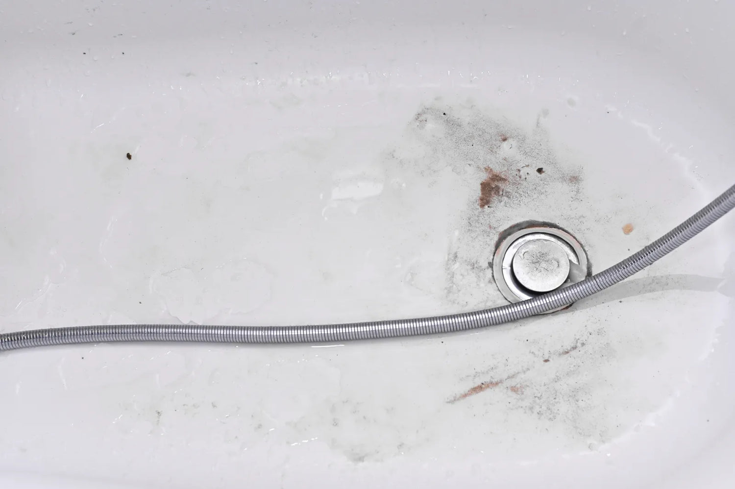 Dirty bathtub drain with black and brown debris near the stopper.