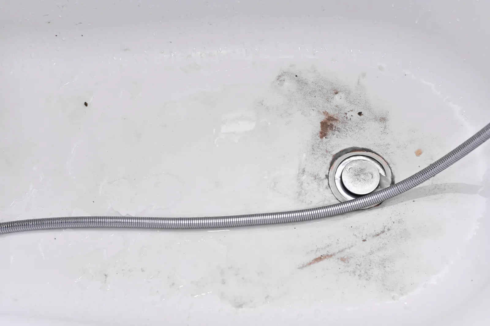Dirty bathtub drain with black and brown debris near the stopper.
