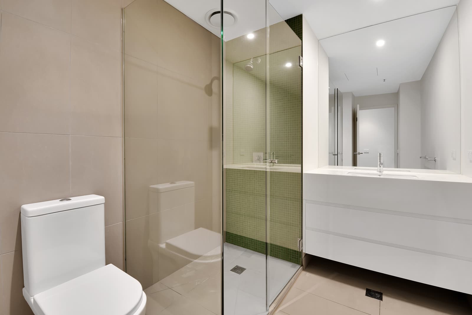 Contemporary neutral-toned bathroom featuring a walk-in shower fitted with a sleek frameless fixed glass panel shower door.