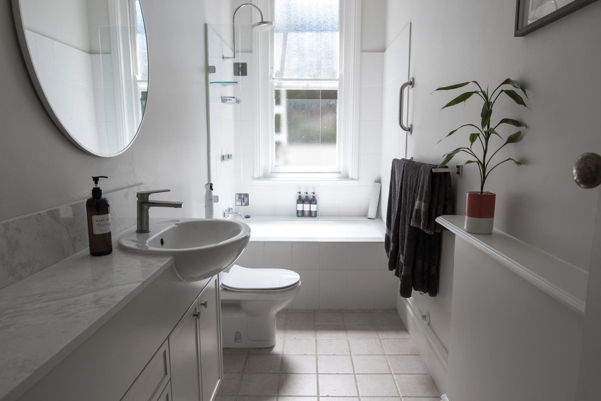 Bright bathroom with a pedestal sink, toilet, bathtub, and marble countertop.