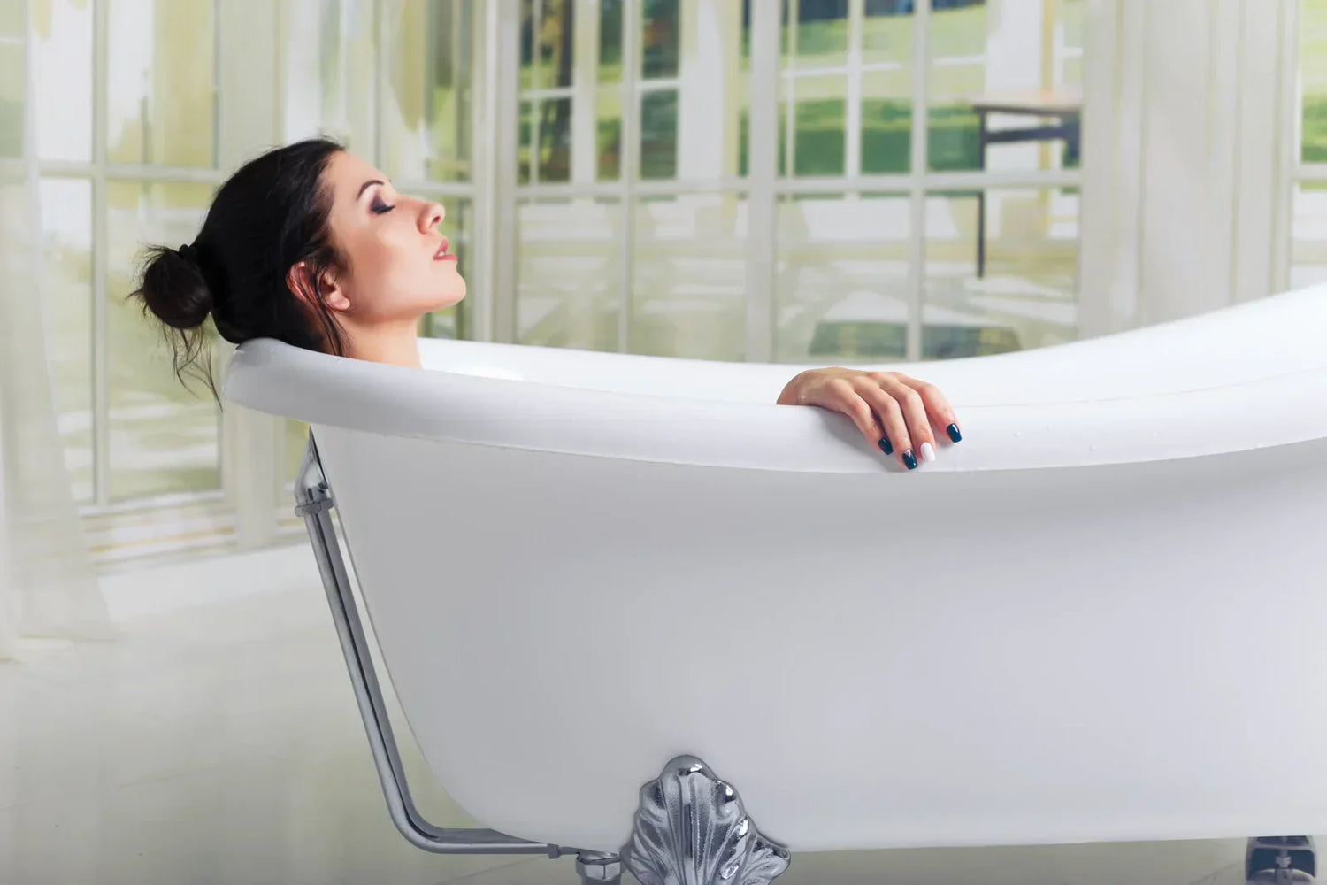 White freestanding clawfoot bathtub used in bright home bathroom for woman to relax and enjoy a comfortable soaking experience