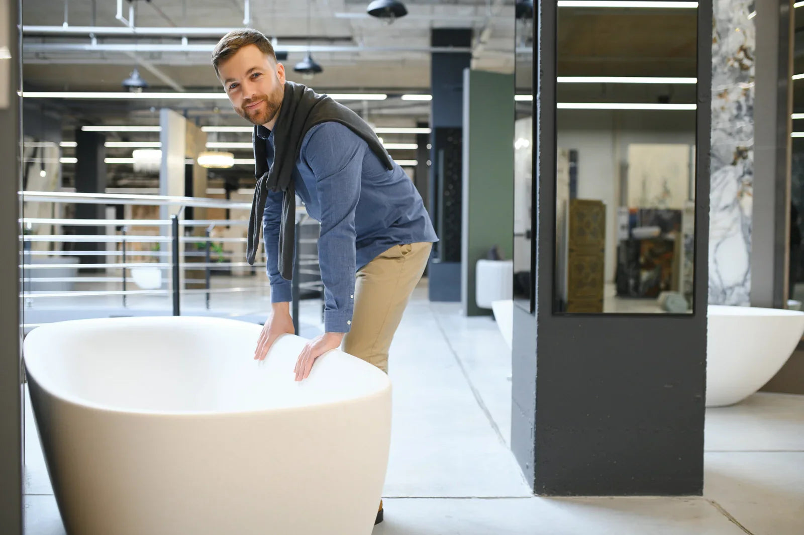 Man inspecting a white freestanding bathtub in a home improvement store for evaluating product quality and suitability before purchase