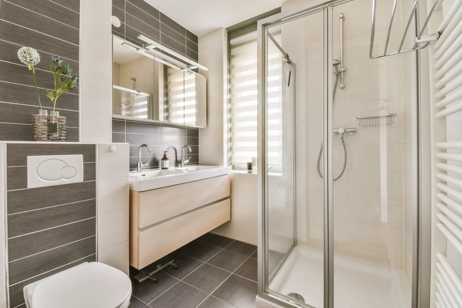 Modern bathroom with toilet, double sink, and glass shower enclosure, lit by natural light.
