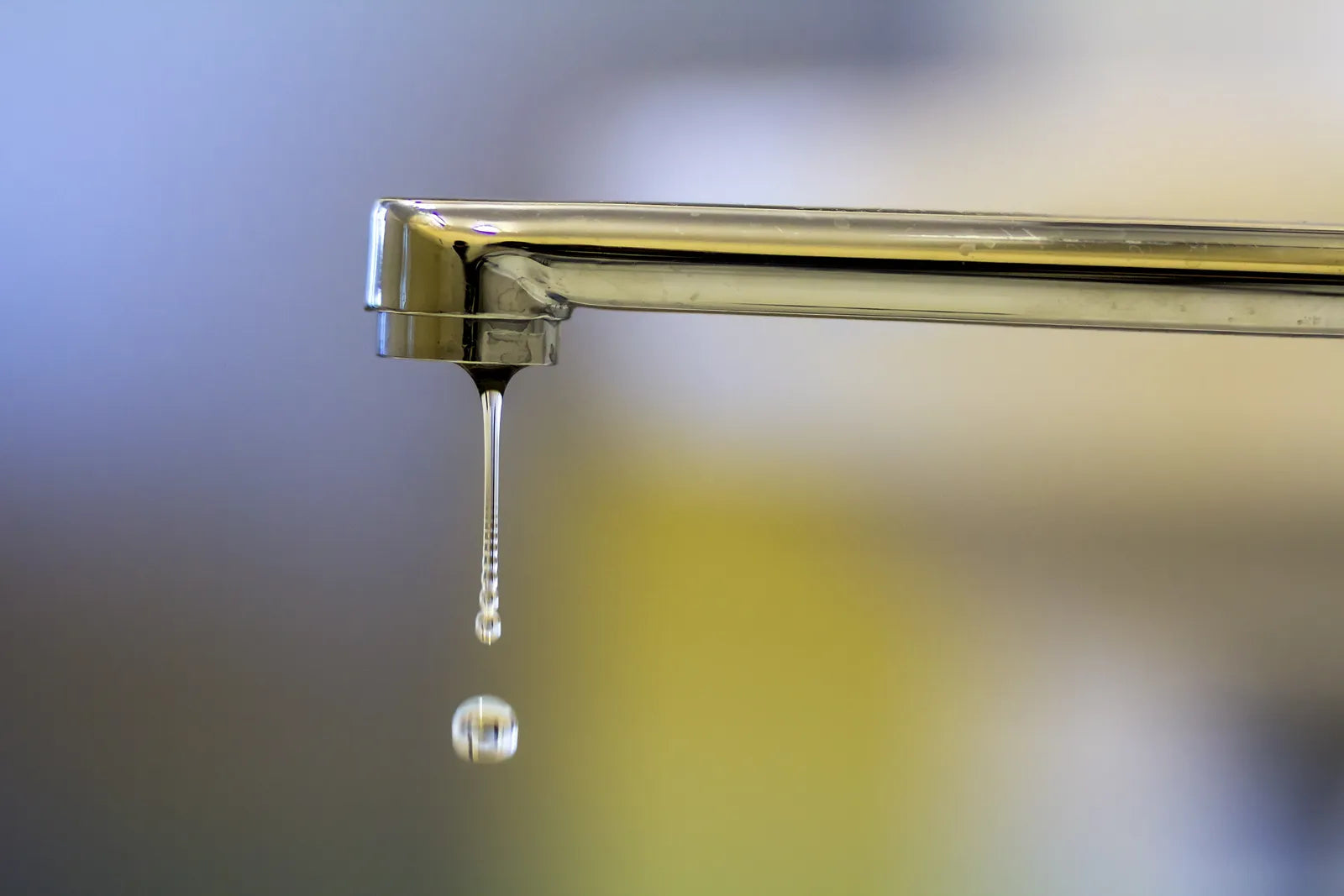 Close-up of a kitchen faucet spout dripping water, showing a leak