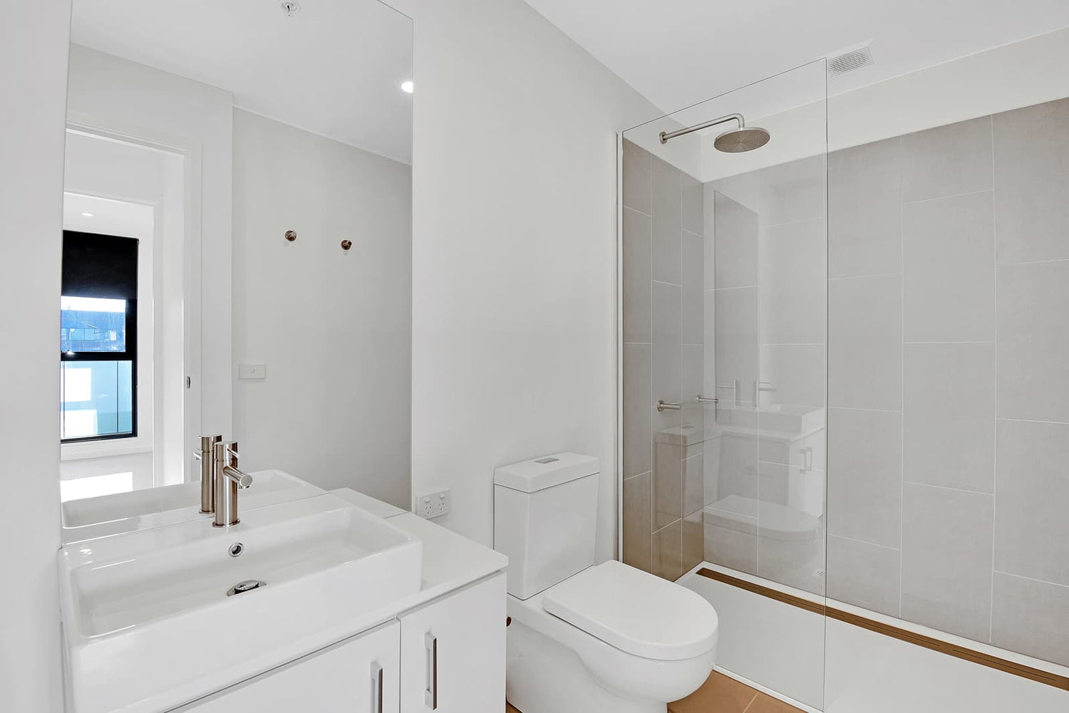 Bright minimalist bathroom with frameless clear glass shower partition, showcasing ultra-clear low iron glass paired with light grey wall tiles.