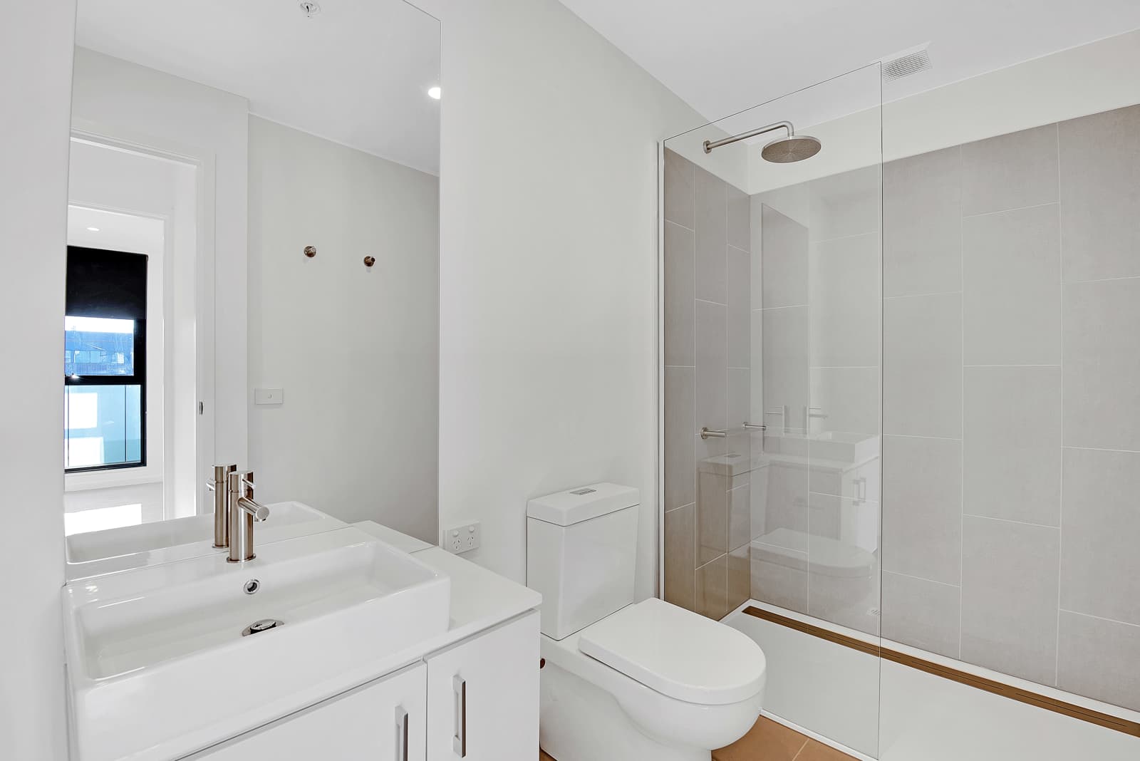 Bright minimalist bathroom with frameless clear glass shower partition, showcasing ultra-clear low iron glass paired with light grey wall tiles.