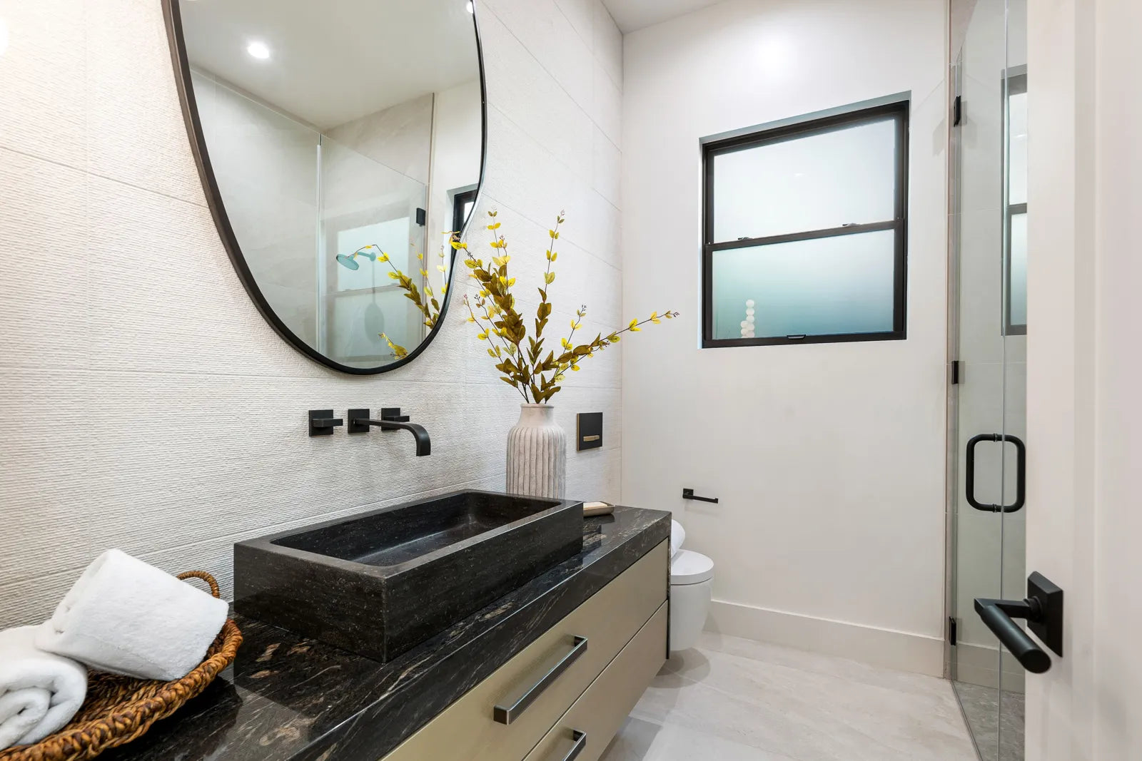Modern bathroom with a matte black stone vessel sink, contrasting with white walls to highlight the bold, contemporary sink choice.