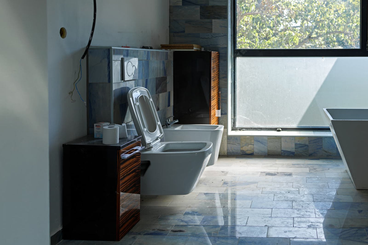 Modern bathroom with wall-hung toilet and bidet beside a large window and tiled floor