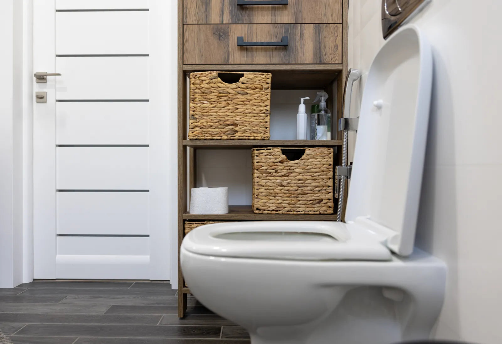 Toilet area with wooden storage unit and woven baskets, demonstrating a smart toilet setup in a humid-resistant bathroom design.