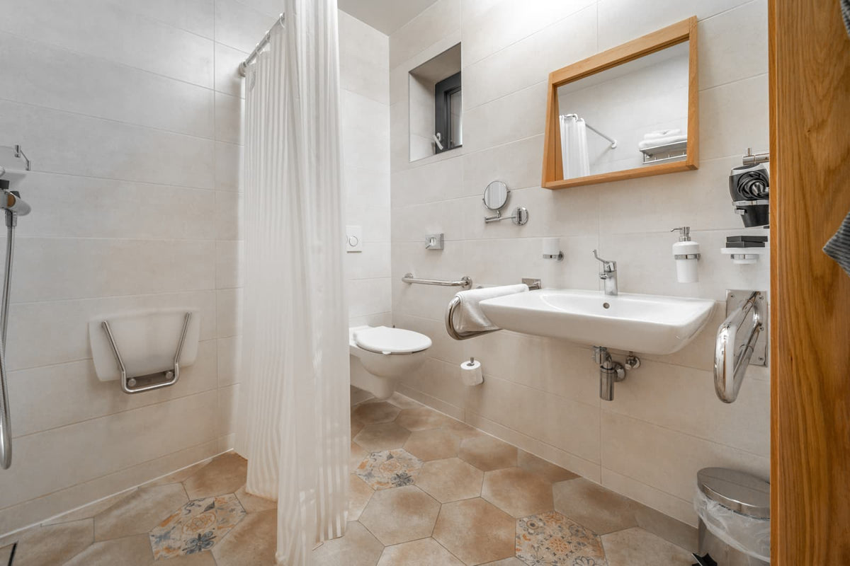 Accessible bathroom with wall-mounted toilet, sink, grab bars, and shower curtain