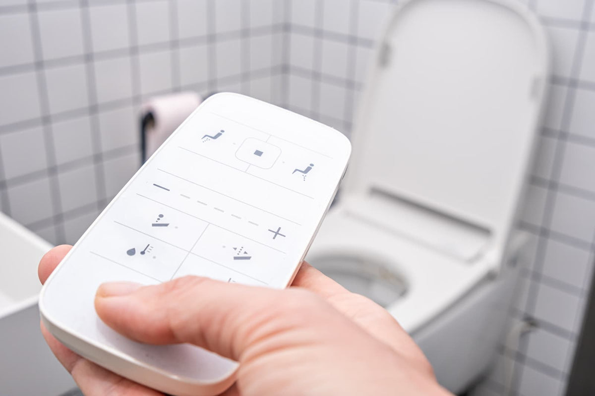 Hand holding a remote control for a smart toilet with heated seat and bidet functions