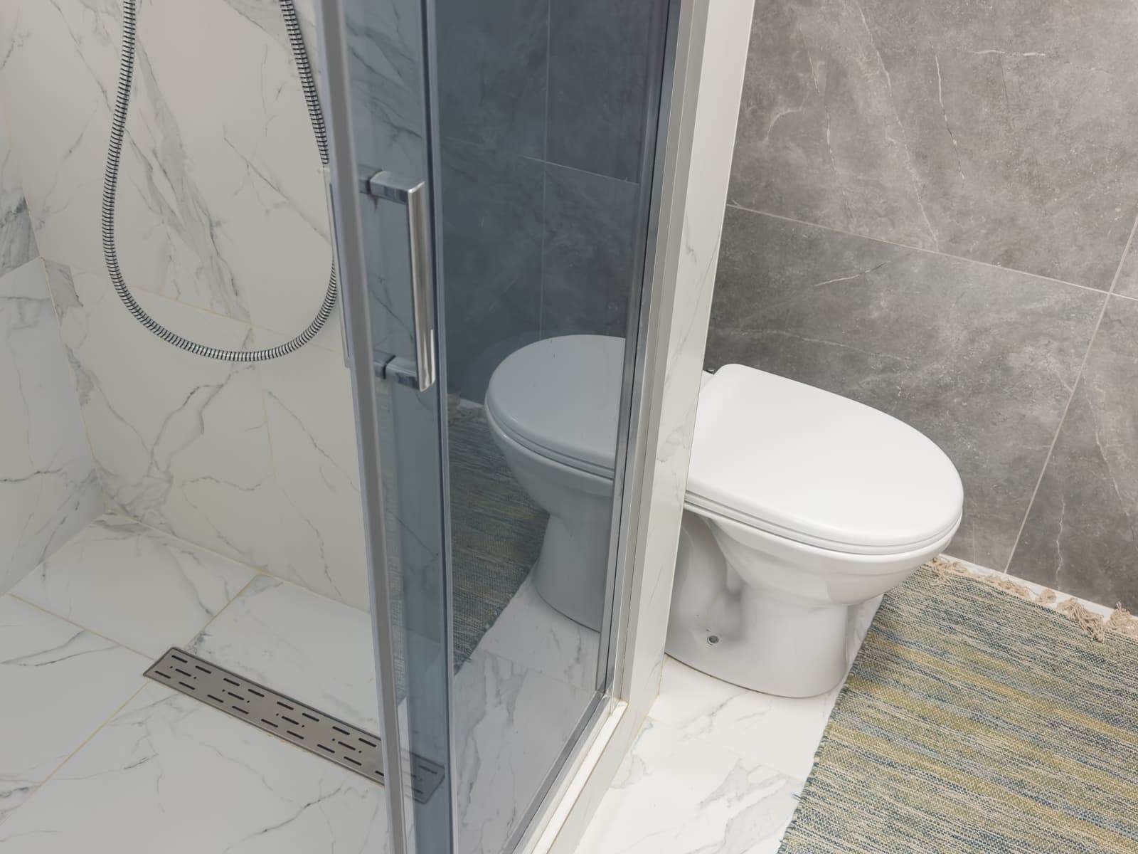 Modern bathroom with sliding tinted glass shower enclosure positioned beside the toilet, showing space planning for compact layouts.