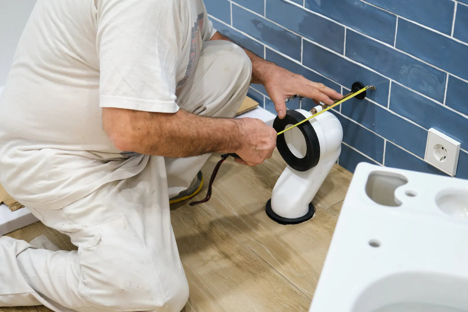 A technician measuring the distance between a toilet’s drain outlet and the water supply valve with a tape measure to ensure proper alignment before installation.