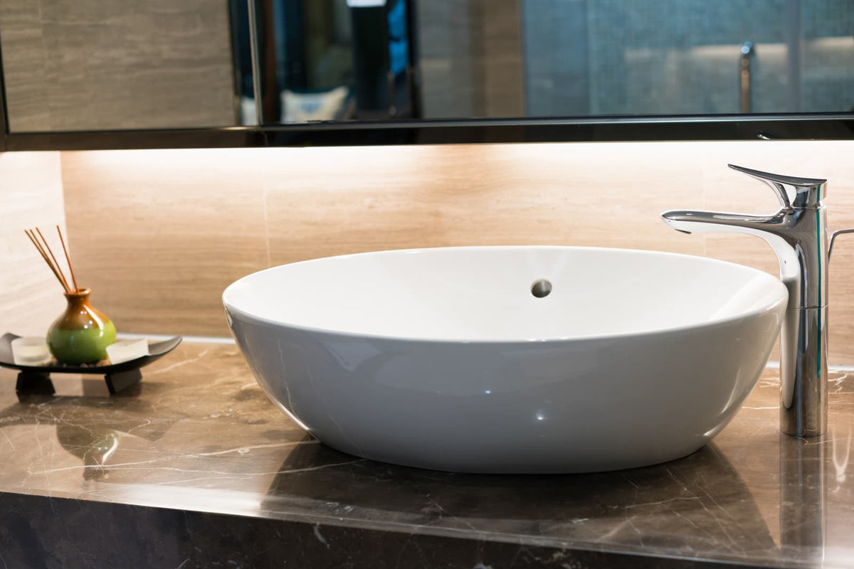 Modern chrome vessel sink faucet beside a white round basin on a marble countertop.